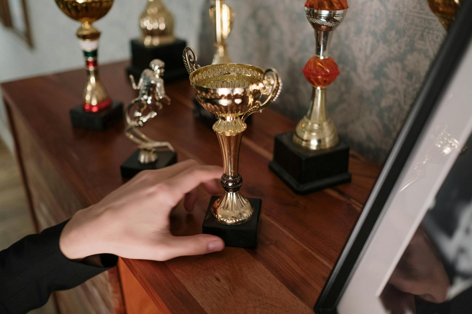 Dłoń sięgająca po błyszczącą statuetkę na drewnianej półce