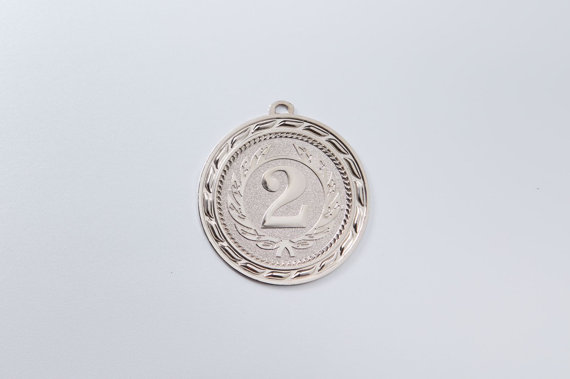 Personalizowane medale sportowe – pomysły na grawer, które zapadają w pamięć Srebrny medal za drugie miejsce z wygrawerowaną cyfrą 2 na białym tle